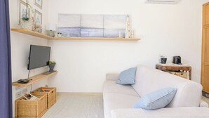 En stue med sofa, fladskærms-tv, kaffemaskine og bogreol.