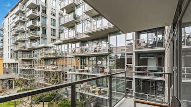 Un edificio residencial de varios pisos con balcones, ventanas amplias y vista a un área ajardinada.