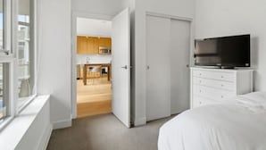 Un dormitorio con una cama, un televisor, un armario y una puerta que da a una cocina.