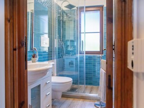 Ein Badezimmer mit Duschkabine aus Glas, einer weißen Toilette und einem Waschbecken mit Schrank.