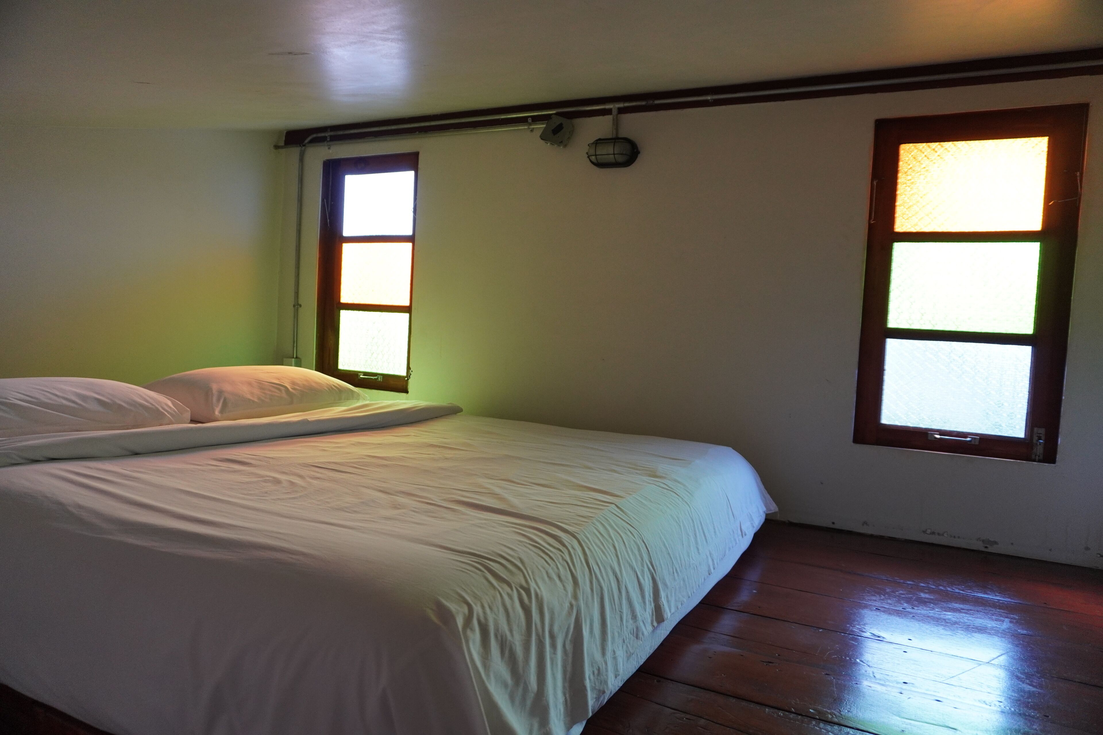 Una cama, una tabla de surf, dos ventanas y suelo de madera.