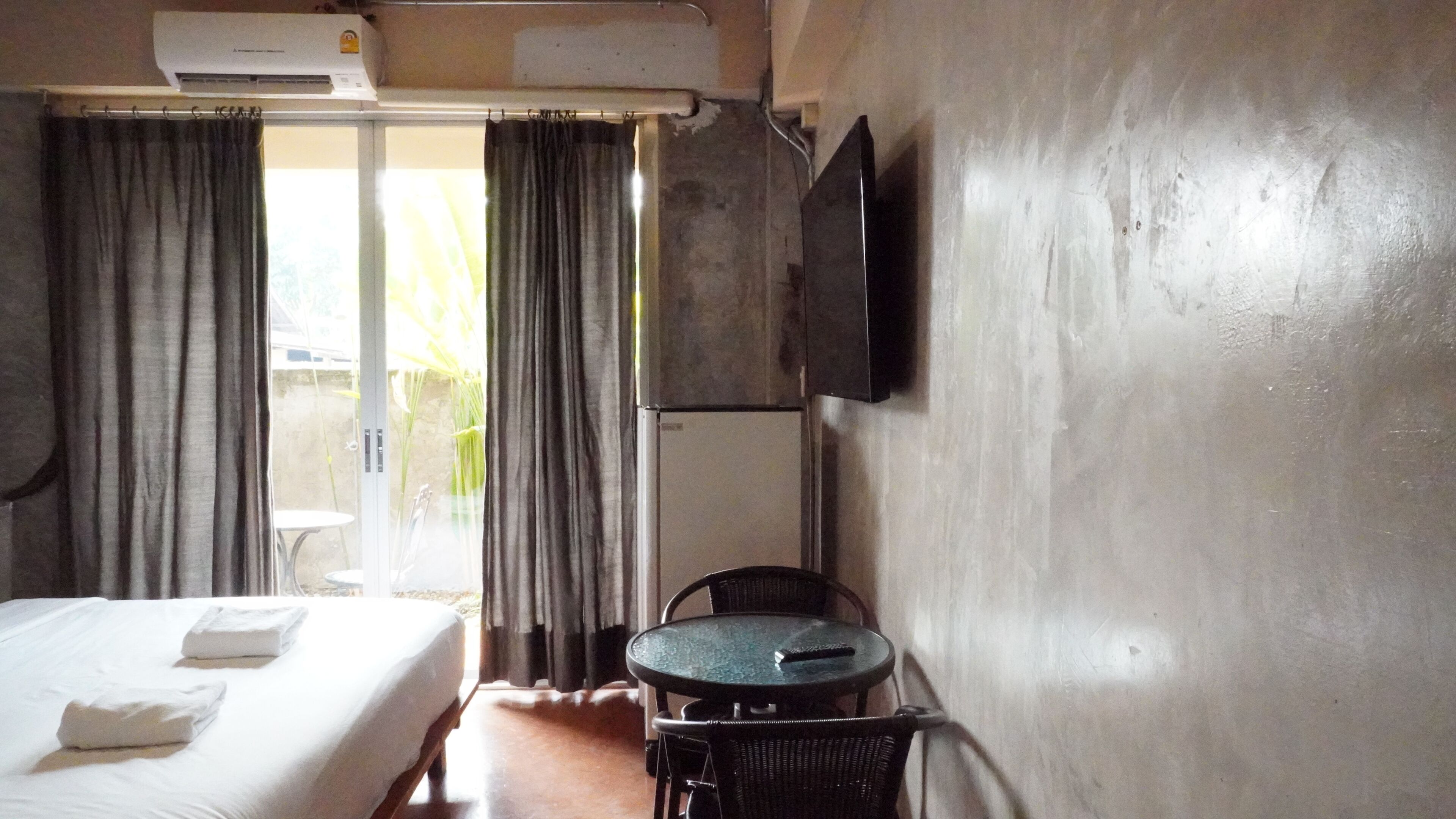 Quarto de hotel com cama, mesa, cadeira, televisão e janela com cortinas.