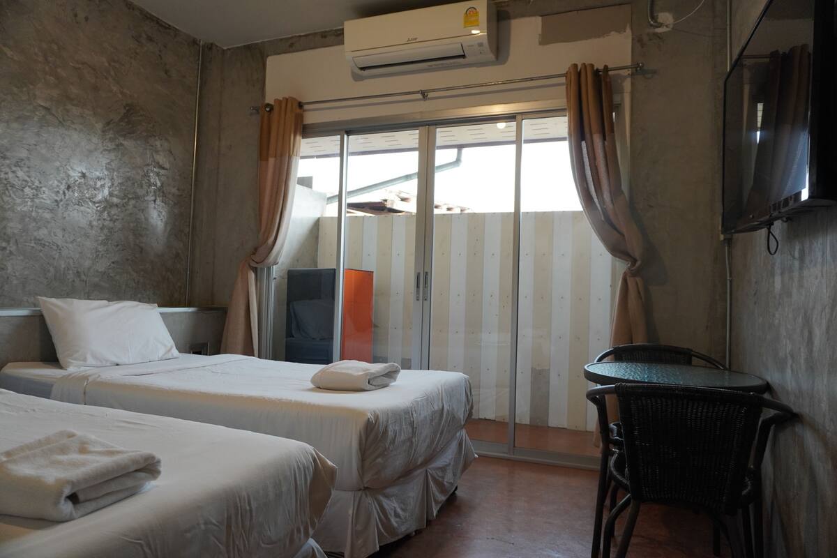 A hotel room with two beds, a small table, a TV, and a sliding glass door.