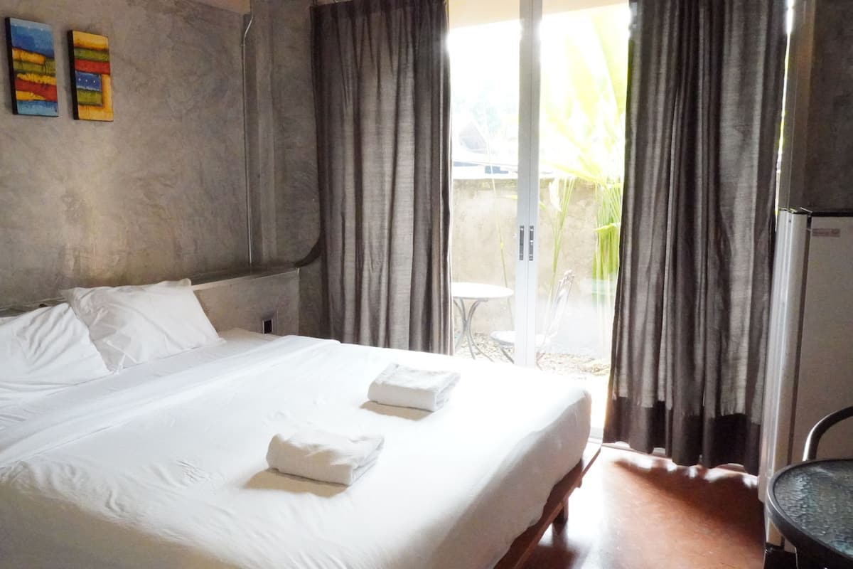 A single-bed room with a large window, a small table, and a chair.