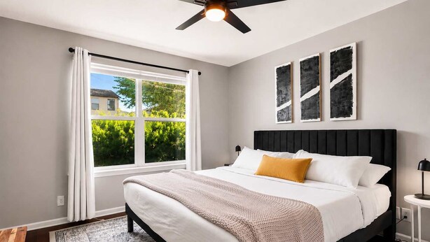 A bedroom with a bed, a ceiling fan, a window with curtains, and a view of greenery outside. - Exclusive Bourbon retreat close to Nulu Downtown! (Louisville)