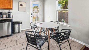 A kitchen with a dishwasher, coffee maker, and trash can. There is a dining table with chairs and a window with a view of a backyard. - Exclusive Bourbon retreat close to Nulu Downtown! (Louisville)