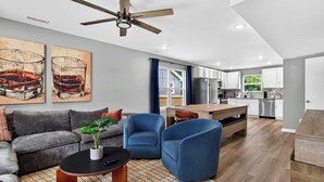 Una sala de estar moderna con un sofá, sillones, una mesa de centro y un ventilador de techo.