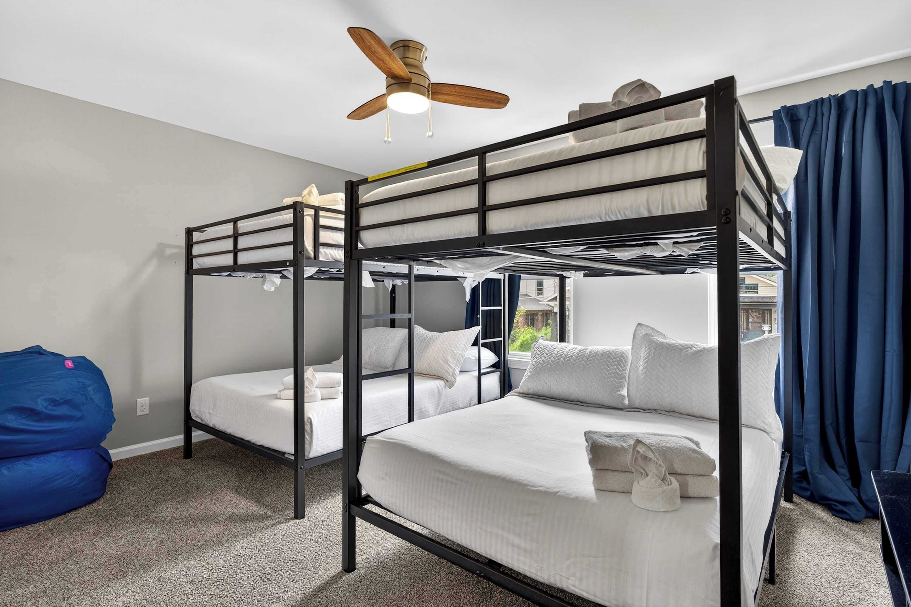 Quarto com beliche, ventilador de teto, um puff azul e vista para o exterior.