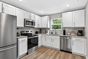 Una cocina moderna con armarios blancos, electrodomésticos de acero inoxidable, una ventana y un salpicadero de azulejos.
