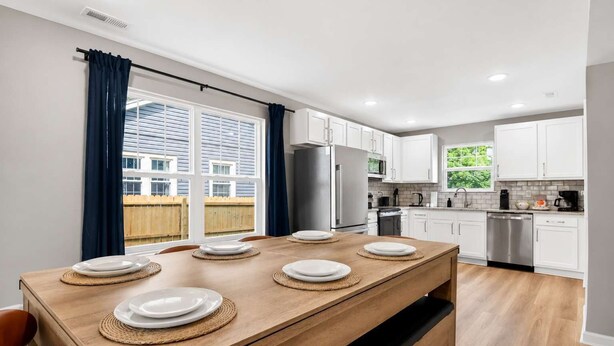 A modern kitchen with white cabinets, stainless steel appliances, and a dining area with a wooden table set for six.