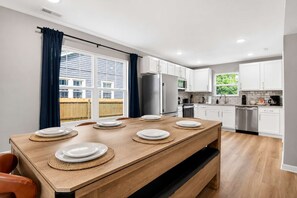 Et moderne køkken med hvide skabe, rustfrie stålapparater og et spiseområde med et træbord dækket til seks.