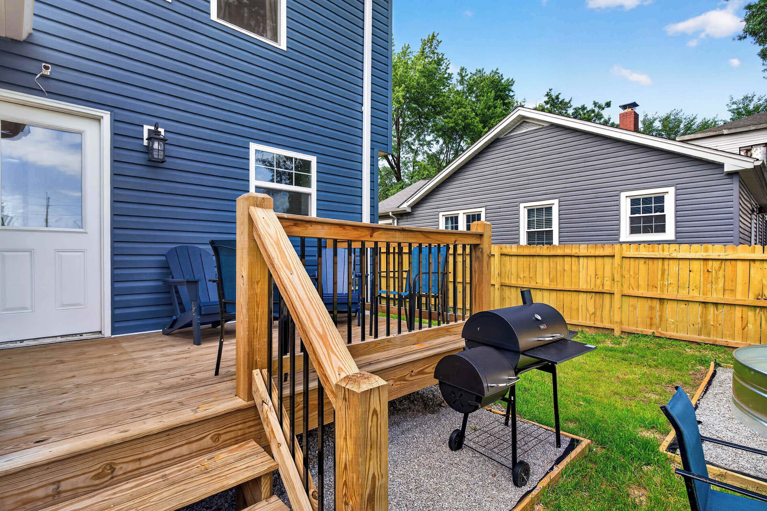 A wooden deck with a barbecue grill, a blue house, and a wooden fence.
