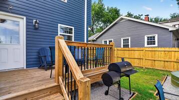 A wooden deck with a barbecue grill, a blue house, and a wooden fence.