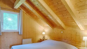 Ein Zimmer mit Holzwänden, einem Bett, einem Nachttisch, einer Lampe und einem Fenster.