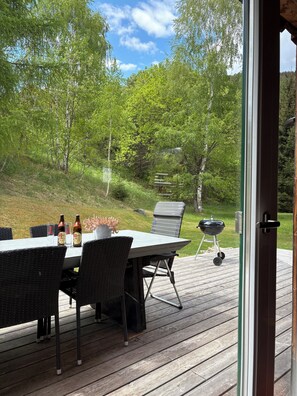 Eine Terrasse im Freien mit Tisch, Stühlen, einem Grill und Blick auf einen bewaldeten Bereich.