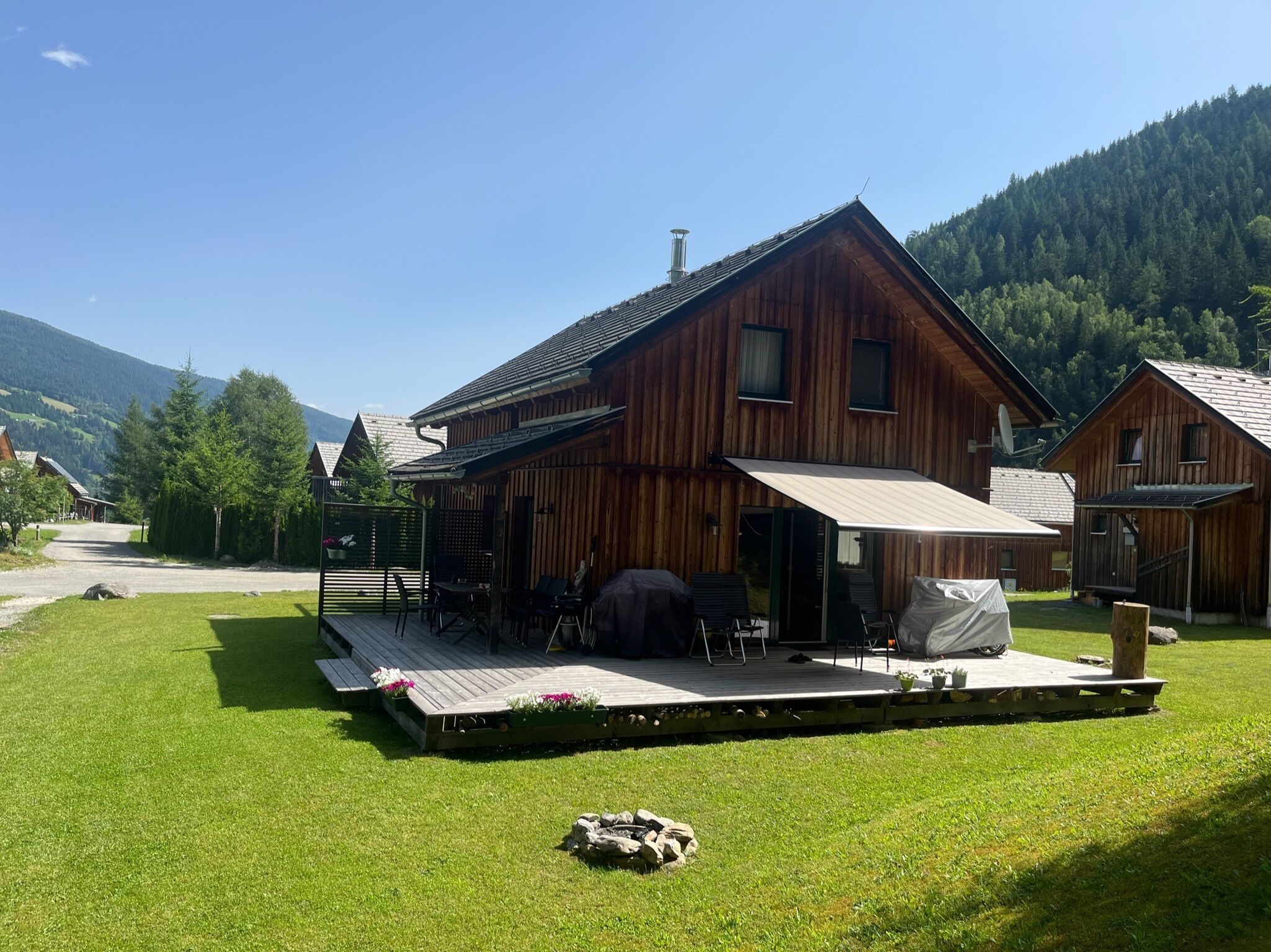 Uma cabana de madeira com varanda, cercada por gramado e montanhas.
