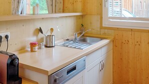 Eine Holzhüttenküche mit Spüle, Kaffeemaschine und einem Fenster mit Vorhängen.