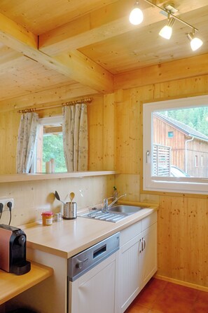 Eine Holzhüttenküche mit Spüle, Kaffeemaschine und einem Fenster mit Vorhängen.