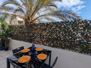 Un área de comedor al aire libre con una mesa lista para cuatro personas, rodeada por una cerca decorativa y palmeras.