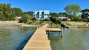 Un molo di legno che si estende verso un pontile su un'area d'acqua, con un grande edificio blu sullo sfondo.