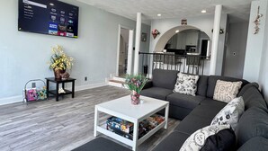 Un soggiorno moderno con una TV a schermo piatto, un divano, un tavolino da caffè e, sullo sfondo, una zona cucina.