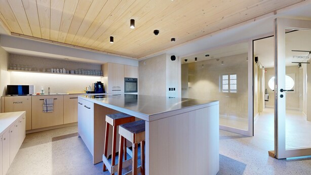 Una cocina moderna con una isla central, electrodomésticos integrados y un comedor con paredes de vidrio.
