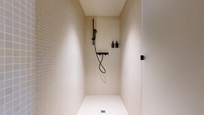 Un espacio de ducha estrecho con azulejos, un cabezal de ducha de mano y un grifo empotrado.
