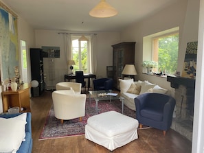 Ein Wohnzimmer mit einer Couch, Sesseln, einem Couchtisch, einem Kamin und Blick auf Grünfläche.