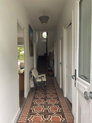 Ein Korridor mit gemustertem Boden, einem Sessel, einem Kleiderständer und einer Treppe zu einem anderen Raum.
