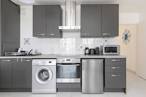 Eine moderne Küche mit grauen Schränken, einer Waschmaschine, einem Backofen, einer Mikrowelle und einem Kühlschrank.