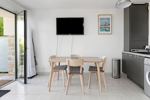 Eine moderne Küche mit eingebautem Geschirrspüler, einem flachbildfernseher an der Wand und einem Essbereich mit Holztisch und Stühlen.