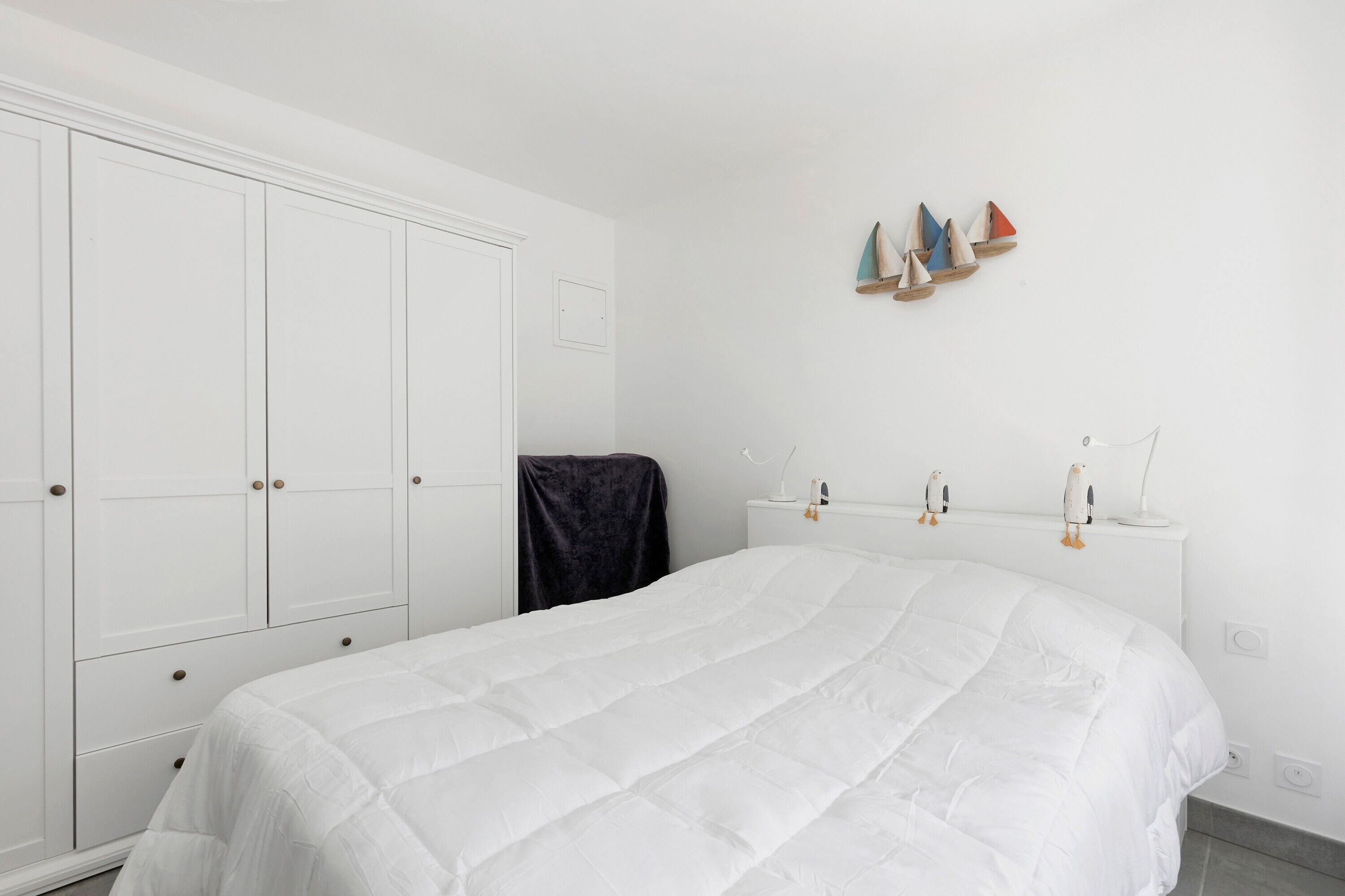 A bedroom with a white bed, a wardrobe, and a nightstand with decorative items.
