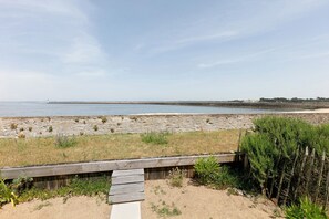 Vista costera con muelle de madera, playa arenosa y un faro distante.
