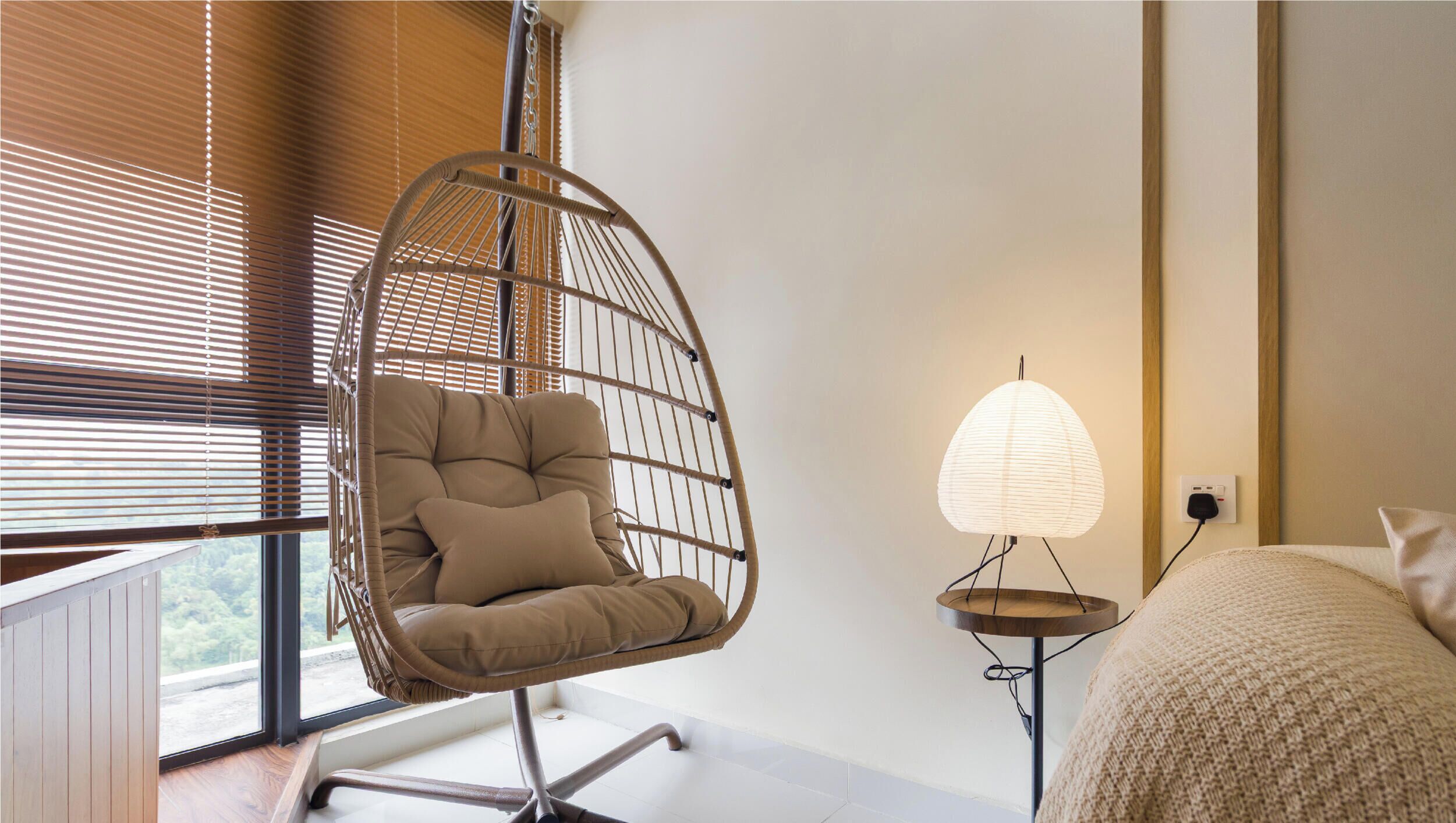 A modern room with a hanging chair, a bedside lamp, and a view through large windows.