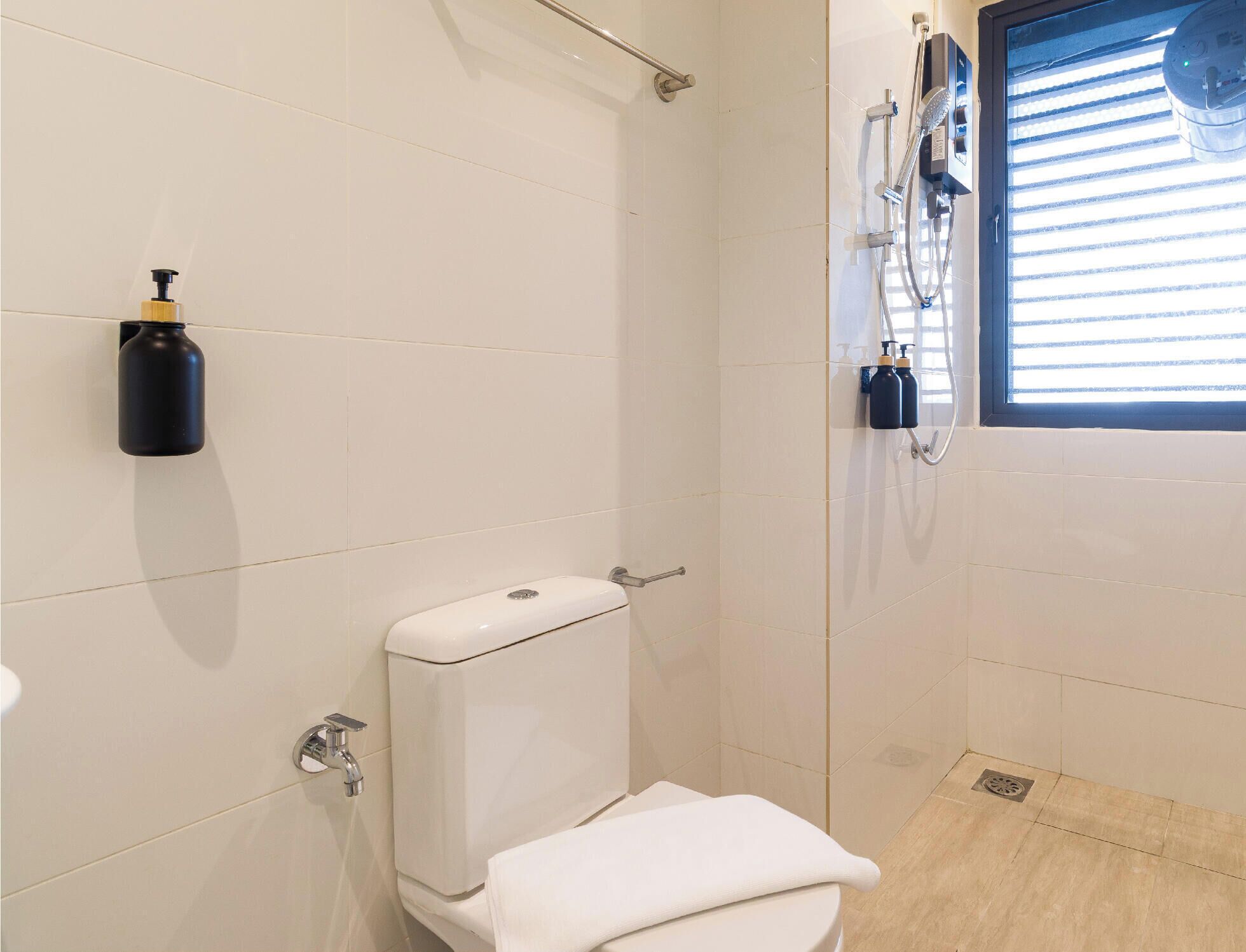 A bathroom with a toilet, a towel, a hand dryer, and a window with blinds.