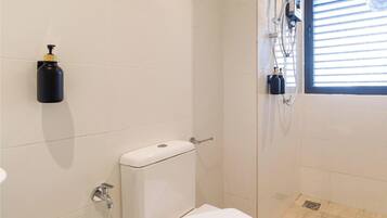 A bathroom with a toilet, a towel, a hand dryer, and a window with blinds.
