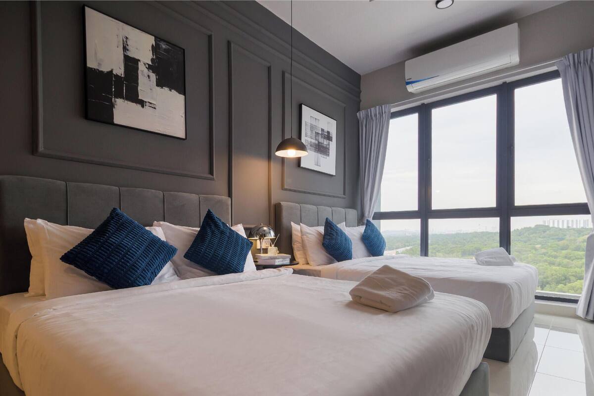 A hotel room with two beds, a large window with a city view, an air conditioning unit, and a framed picture on the wall.