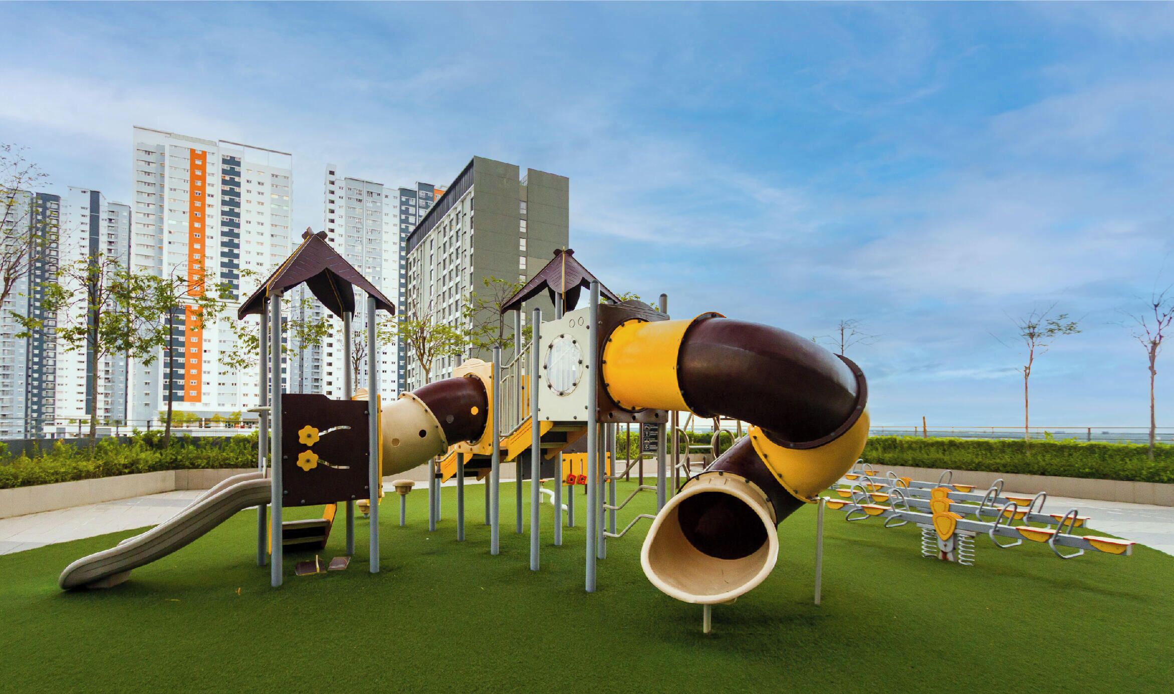 A playground with slides and climbing structures, surrounded by green grass and a clear sky.
