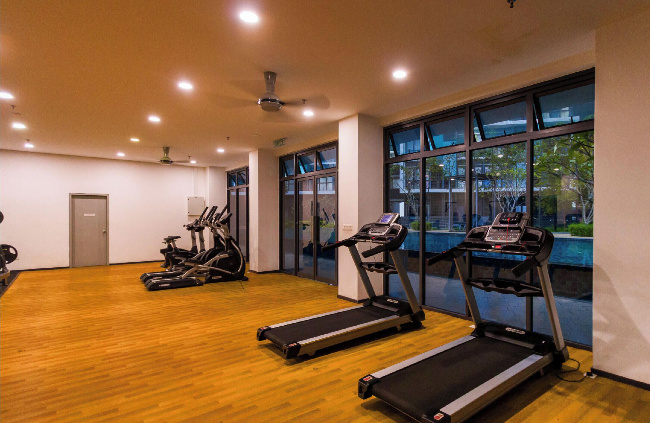 A gym with treadmills, stationary bikes, and a wooden floor.