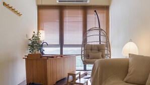 Una habitación con un escritorio de madera, una silla colgante, un sofá y una ventana con persianas.