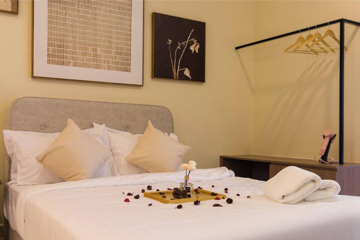 A neatly made bed with pillows, a bedside table with a candle, and a tray with flowers and pine cones.