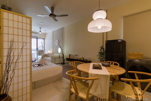 A modern living room with a sofa, a dining table with chairs, a ceiling fan, and a washing machine.