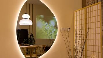 A room with a round mirror reflecting a dining area, a projection screen displaying a nature scene, and a traditional Japanese screen.