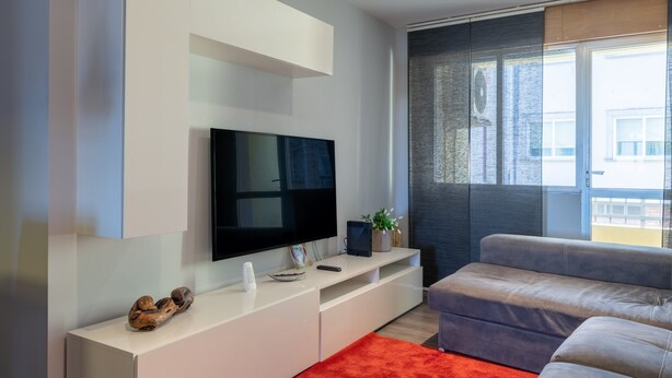 A modern living room with a flat-screen TV, white entertainment unit, grey sofa, and a red rug. - Vacation Apartment in O Grove with Wi-Fi and Air Conditioning (O Grove)
