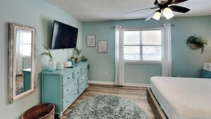 A bedroom with a bed, a dresser, a television, a ceiling fan, and a window with blinds. - Lagoon Sun #7 | One Block from the Beach! (Gulf Shores)