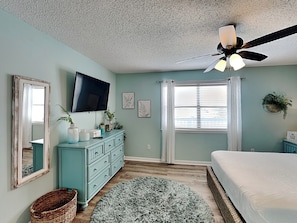 A bedroom with a bed, a dresser, a television, a ceiling fan, and a window with blinds. - Lagoon Sun #7 | One Block from the Beach! (Gulf Shores)