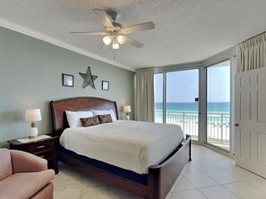 A bedroom with a bed, nightstands, a ceiling fan, a star decoration, and a view of the beach. - Pearl of Navarre 406 | Resort Amenities + Walking Distance to Dining/Fun (Navarre Beach)