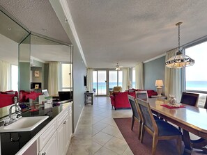 A hotel room with a kitchen, dining area, and a view of the ocean. - Pearl of Navarre 406 | Resort Amenities + Walking Distance to Dining/Fun (Navarre Beach)