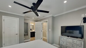 Een slaapkamer met een bed, een plafondventilator, een televisie en een dressoir.