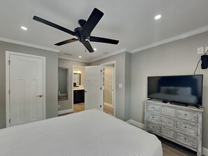 Ein Schlafzimmer mit Bett, Deckenventilator, Fernseher und Kommode.